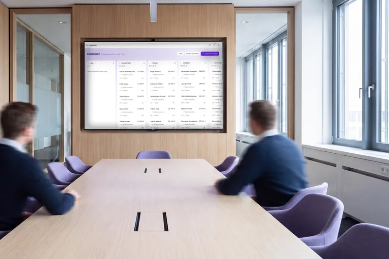 Zwei Personen von hinten im Besprechungsraum vor einem Wandbildschirm, darauf das Dealphasen-Board von ClosingHub mit offenen Deals je Stufe